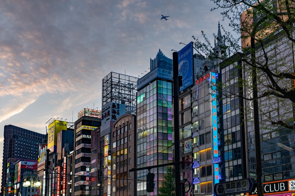 Shinjuku Fassaden im Abendlicht mit Flugzeug
